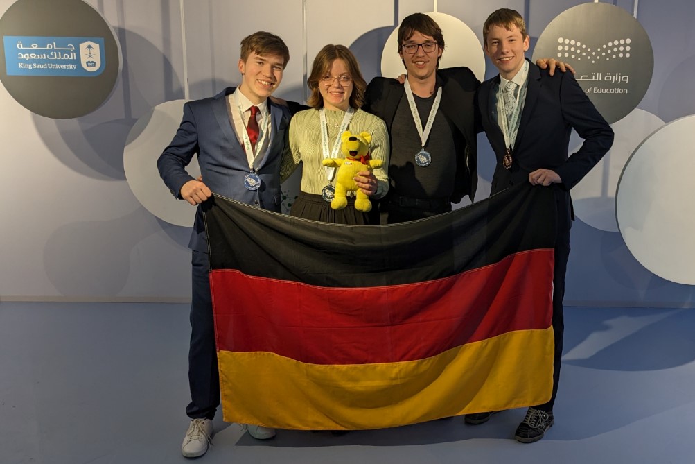 Das deutsche Team der IChO  2024 in Riad. V.l.n.r.: Timur Malikov (silber), Paulina Sievert (silber, mit Maskottchen), Konrad Jannes Köhler (silber), Magnus Güldenpfennig (bronze).